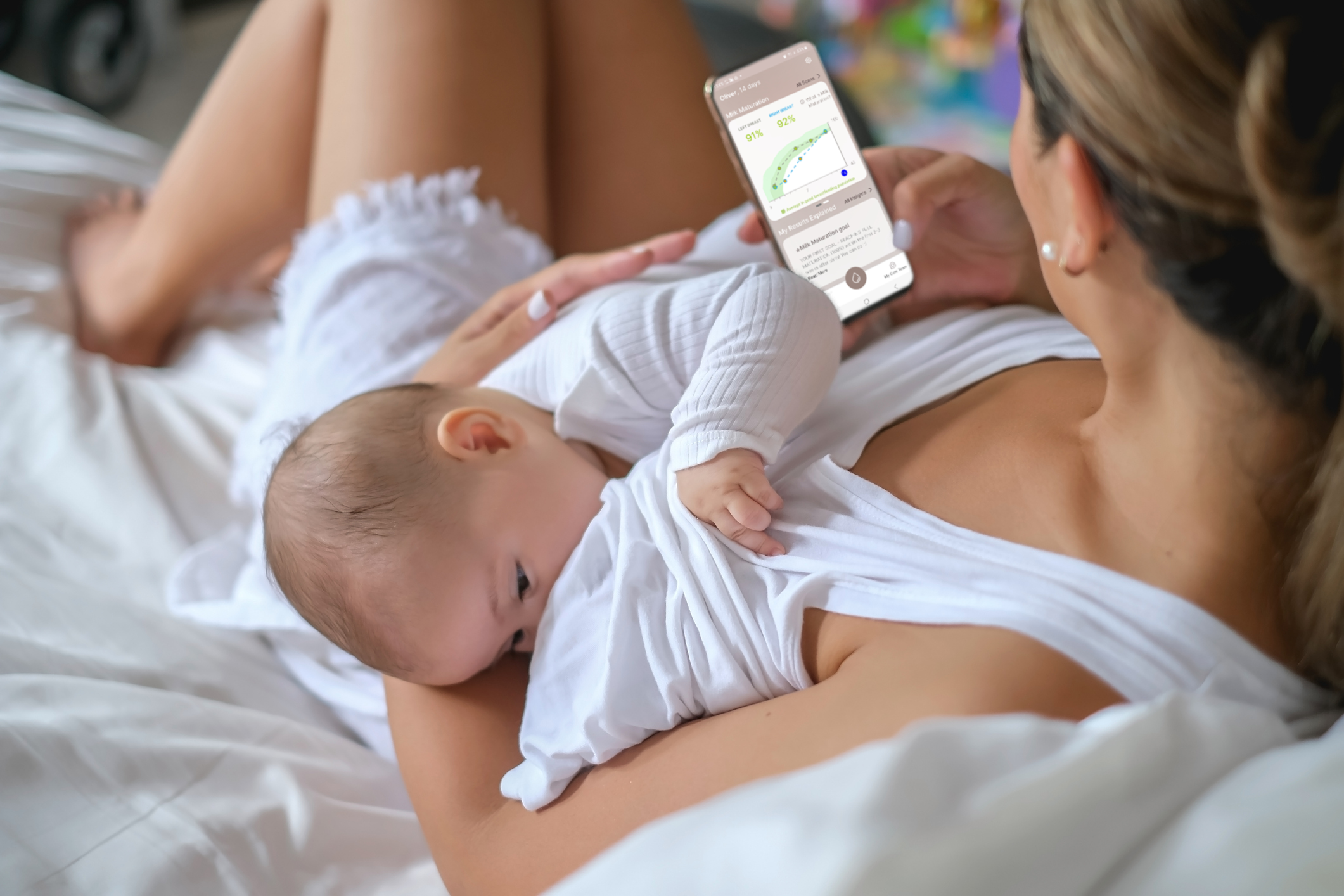 mother breastfeeding while looking at her breastfeeding progress chart on mylee app interface on her phone